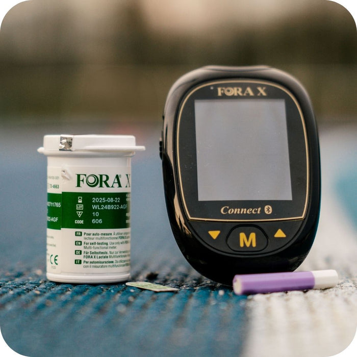 Lecteur de lactate Fora X Connect avec flacon de bandelettes et autopiqueur, posé sur une piste d'athlétisme